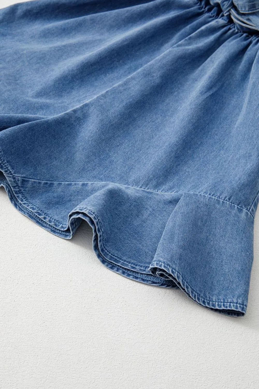 Medium wash denim romper with ruffled hem detail