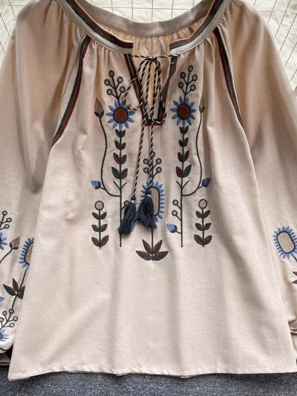 Apricot tie neck blouse with billowy sleeves and intricate floral embroidery.