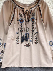 Apricot tie neck blouse with billowy sleeves and intricate floral embroidery.