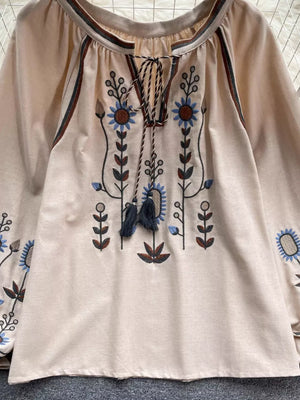 Apricot tie neck blouse with billowy sleeves and intricate floral embroidery.