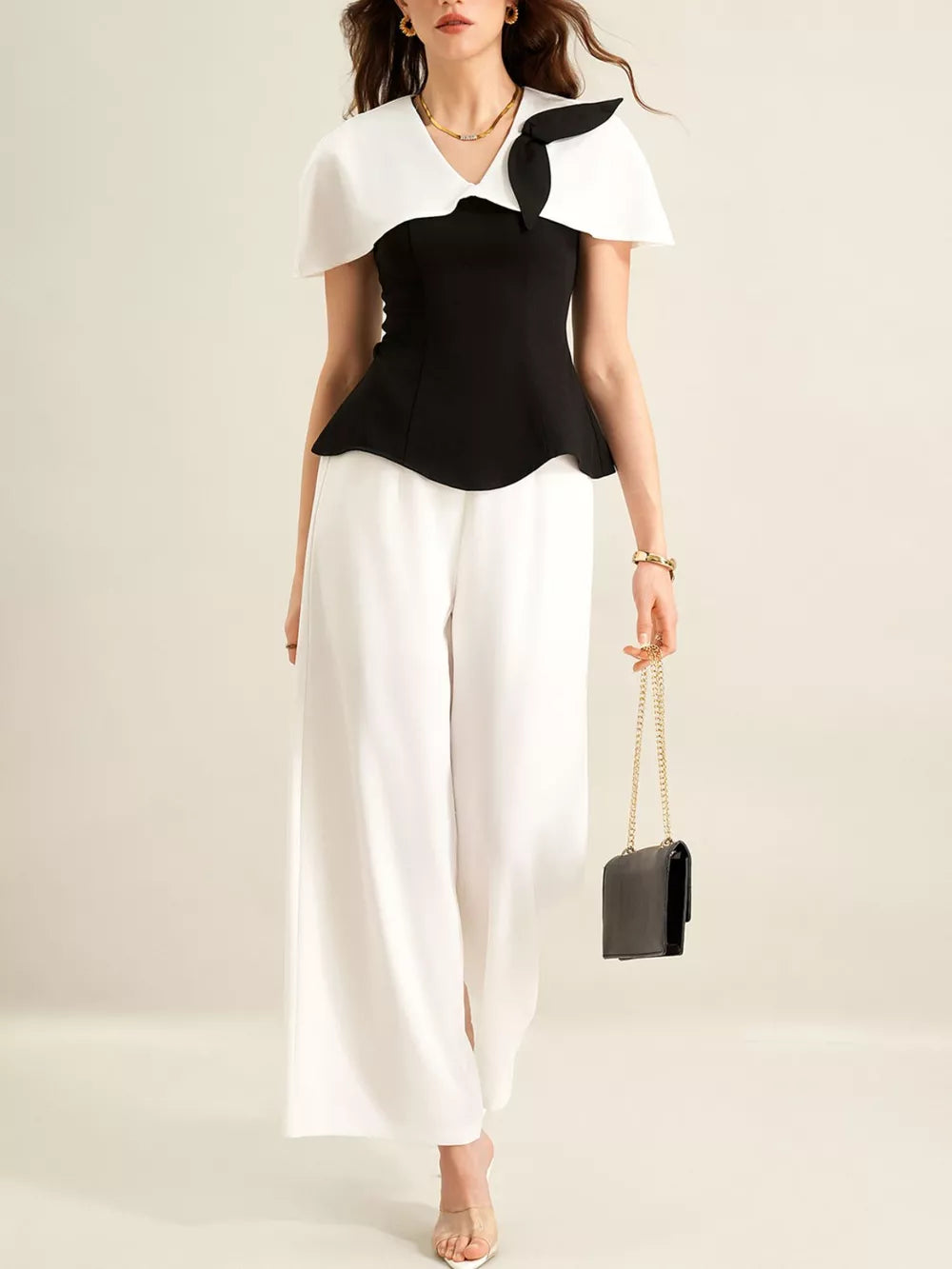 Black peplum top with white cape collar and bow detail, paired with white wide-leg pants.