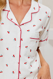 White pajama set with cherry print, red piping, and textured fabric.