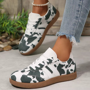 Trendy cow print low-top sneakers with white laces and brown soles.