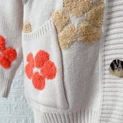 Ivory knit cardigan with embroidered floral appliques and textured details.