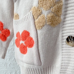 Ivory knit cardigan with embroidered floral appliques and textured details.