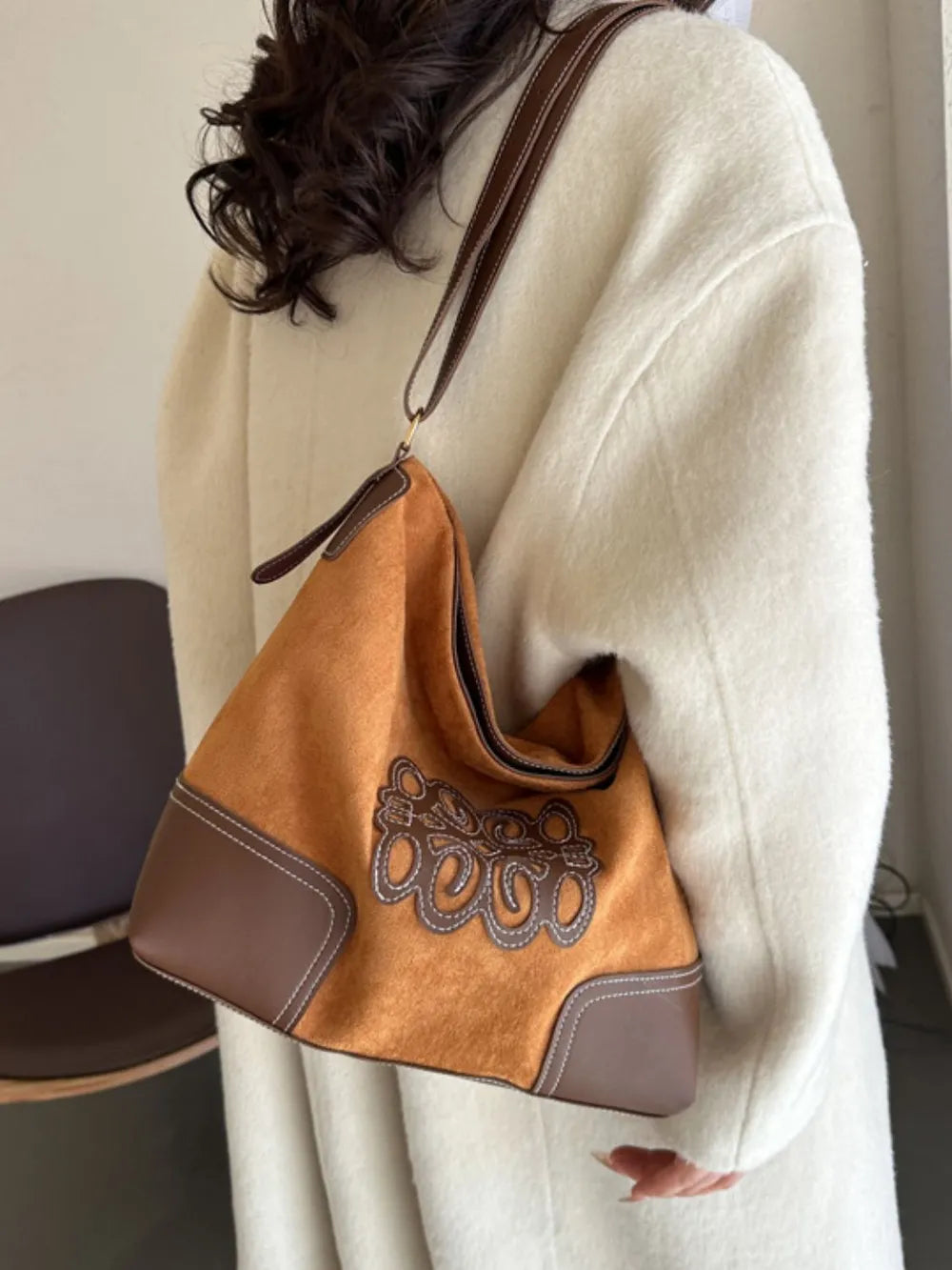 Ochre suede hobo bag with brown leather trim, appliqué detail, and contrast stitching.