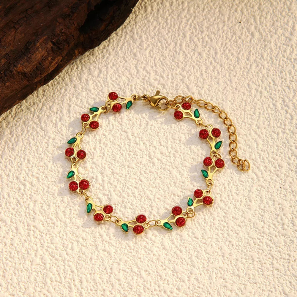 Gold-plated bracelet with red cherry clusters and green leaves, adjustable chain.