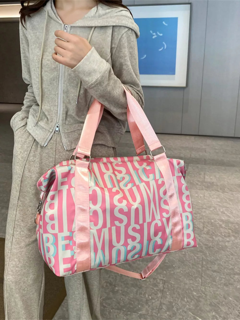 Pink travel bag with all-over white and blue letter print and versatile straps.
