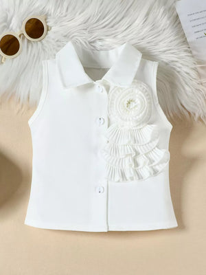 White sleeveless collared blouse with ruffled flower applique and decorative buttons.