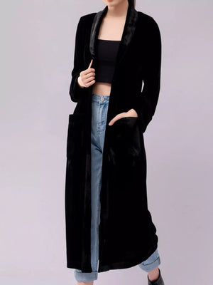 Black velvet longline trench coat with draped lapels and pockets, worn open over a crop top and jeans.