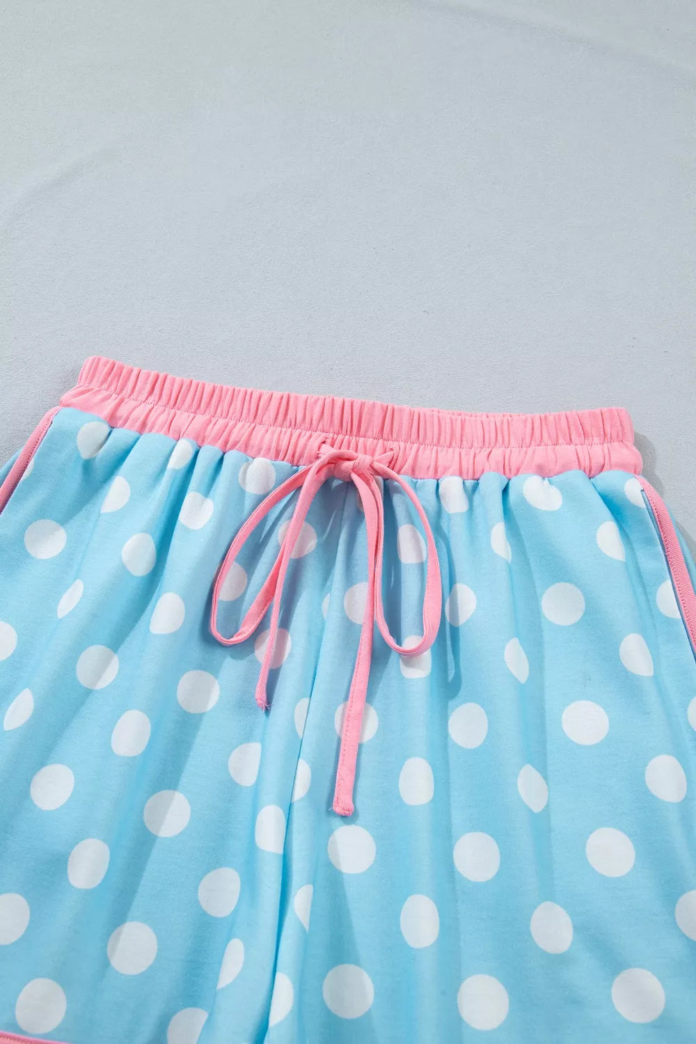 Polka dot pajama shorts in pastel blue polyester with pink drawstring and contrast trim.