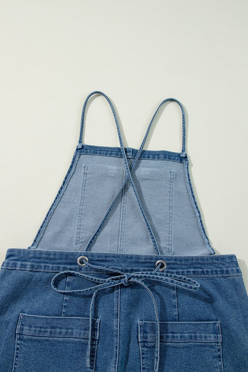 Denim wide-leg overalls in medium wash with adjustable straps and drawstring waist.