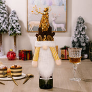 Festive gnome bottle topper with gold sequin hat and reindeer antlers, white beard, and yellow striped sleeves.