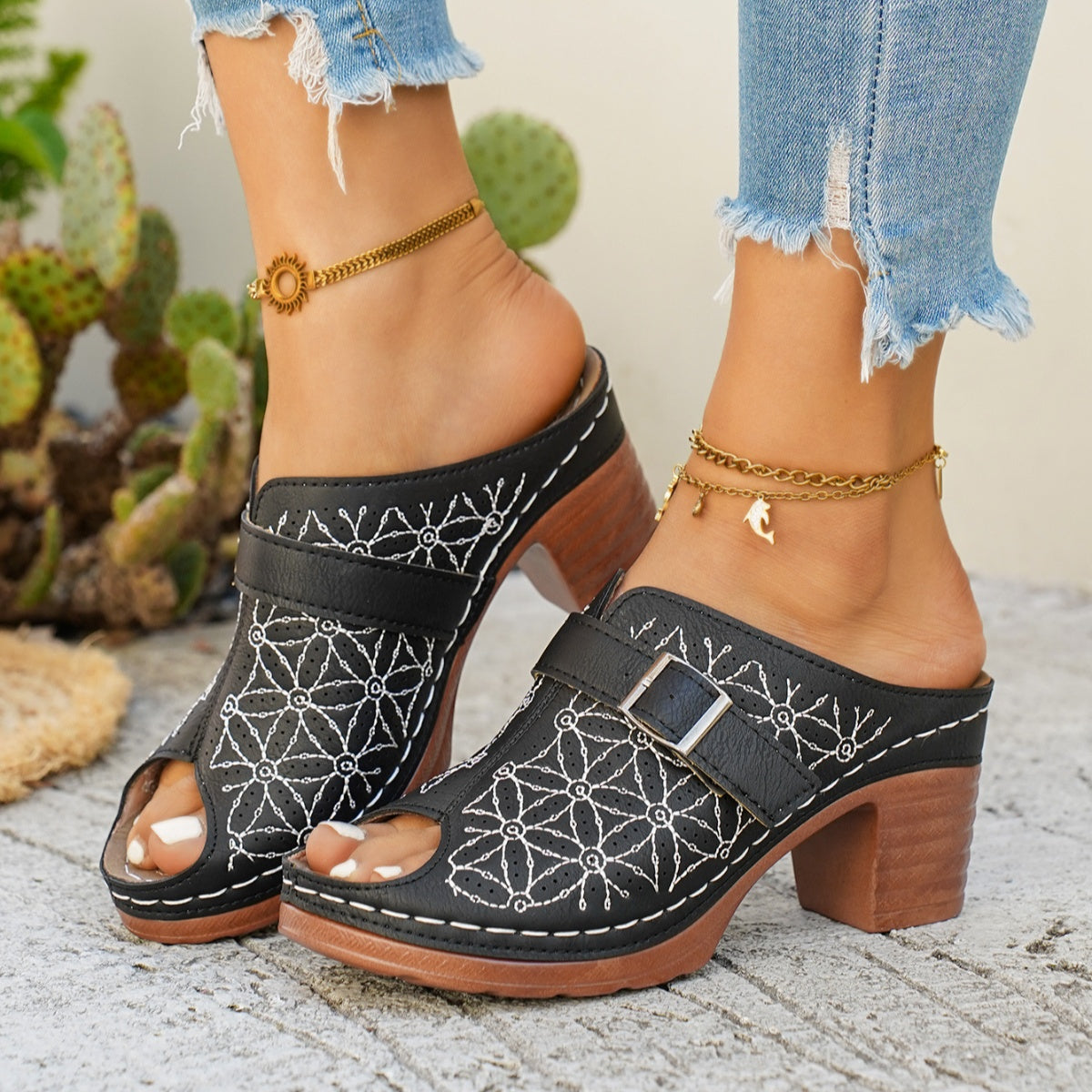 Black peep-toe block heel sandals with white floral embroidery and a buckle detail.