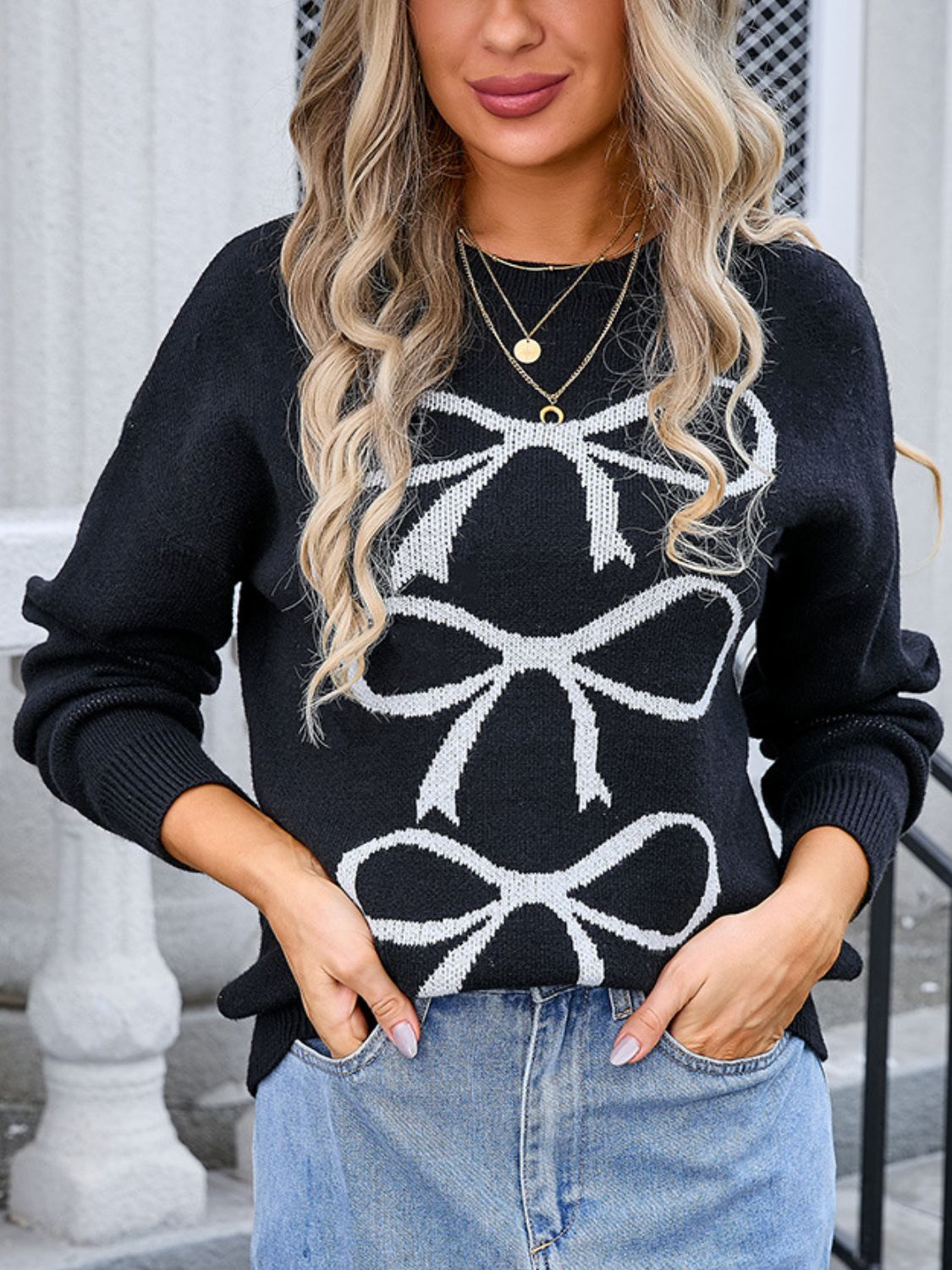 Black knit sweater with white bow motif, crew neck, long sleeves.