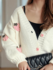 Cream knit cardigan with pink strawberry appliqués and pink buttons.