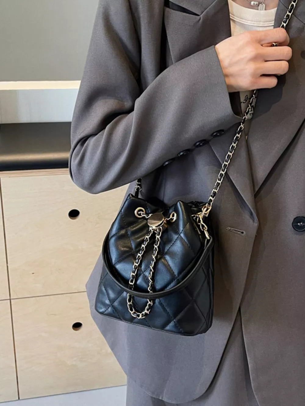 Black quilted bucket bag with chain strap and drawstring closure.