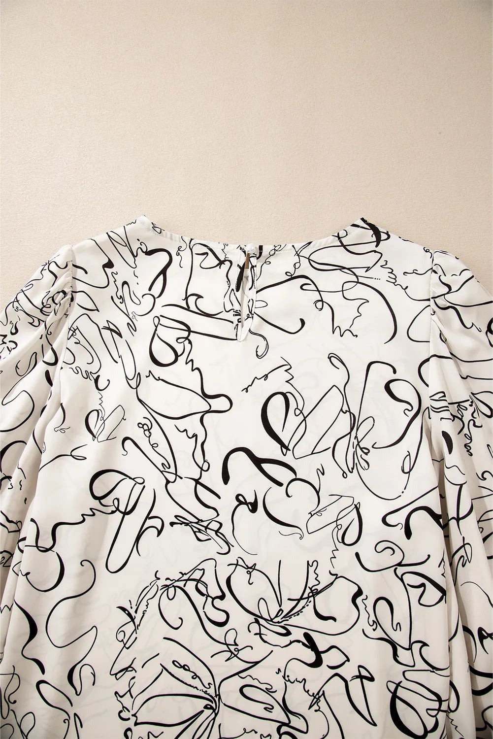 Ivory abstract scribble balloon sleeve blouse with crew neck and back keyhole closure.
