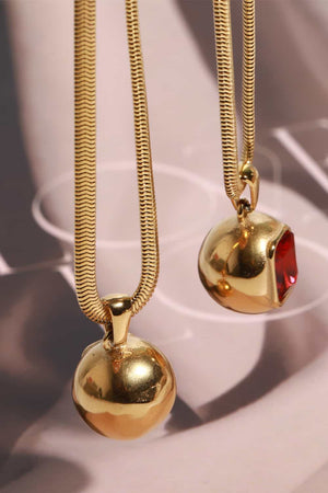 Gold snake chain necklaces with orb and square red stone pendants.