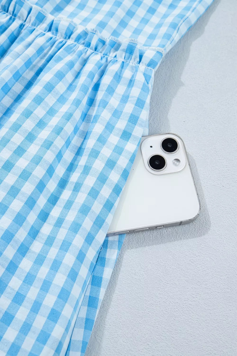 Blue gingham tiered maxi dress with ruffled waist and side pocket holding a phone.