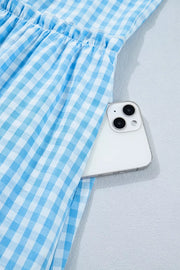 Blue gingham tiered maxi dress with ruffled waist and side pocket holding a phone.
