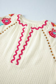 Beige embroidered blouse with voluminous sleeves and pink zigzag neckline detail.