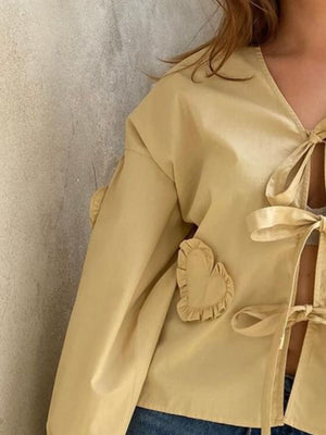 Pastel yellow blouse with tie front, long sleeves, and heart appliqué details.