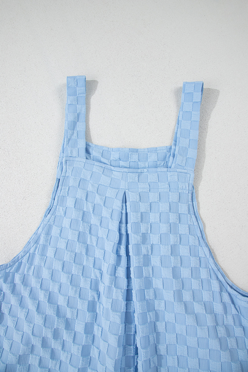 Light blue textured checkered jumpsuit with button straps and wide legs.