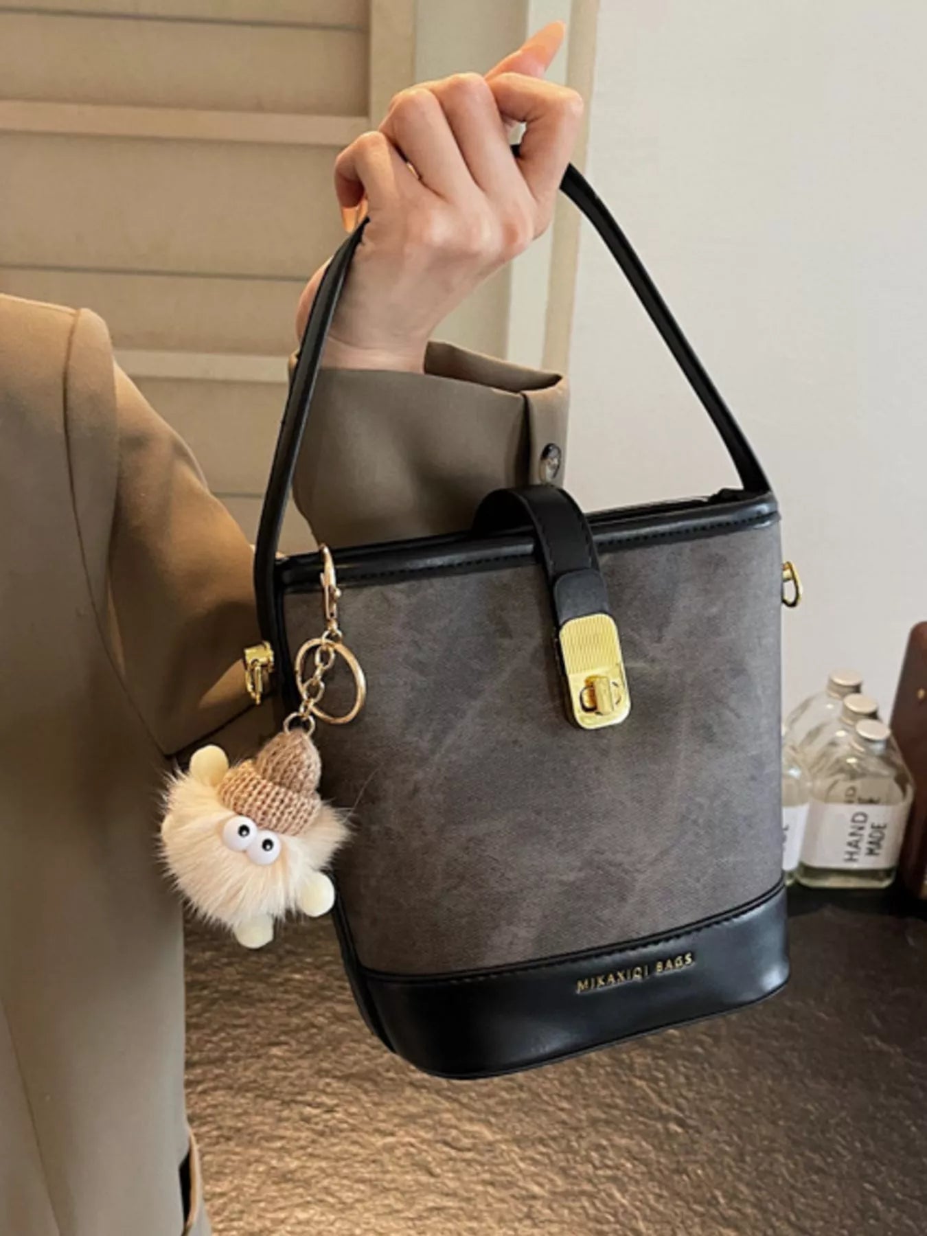 Elegant PU leather bucket bag in dark brown with black trim and gold hardware, featuring a fuzzy charm.
