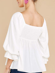 White babydoll blouse with square neckline, smocked back, and ruffled puff sleeves.