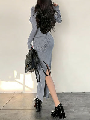 Light gray ruched long-sleeve bodycon maxi dress with a high slit and a black quilted handbag.