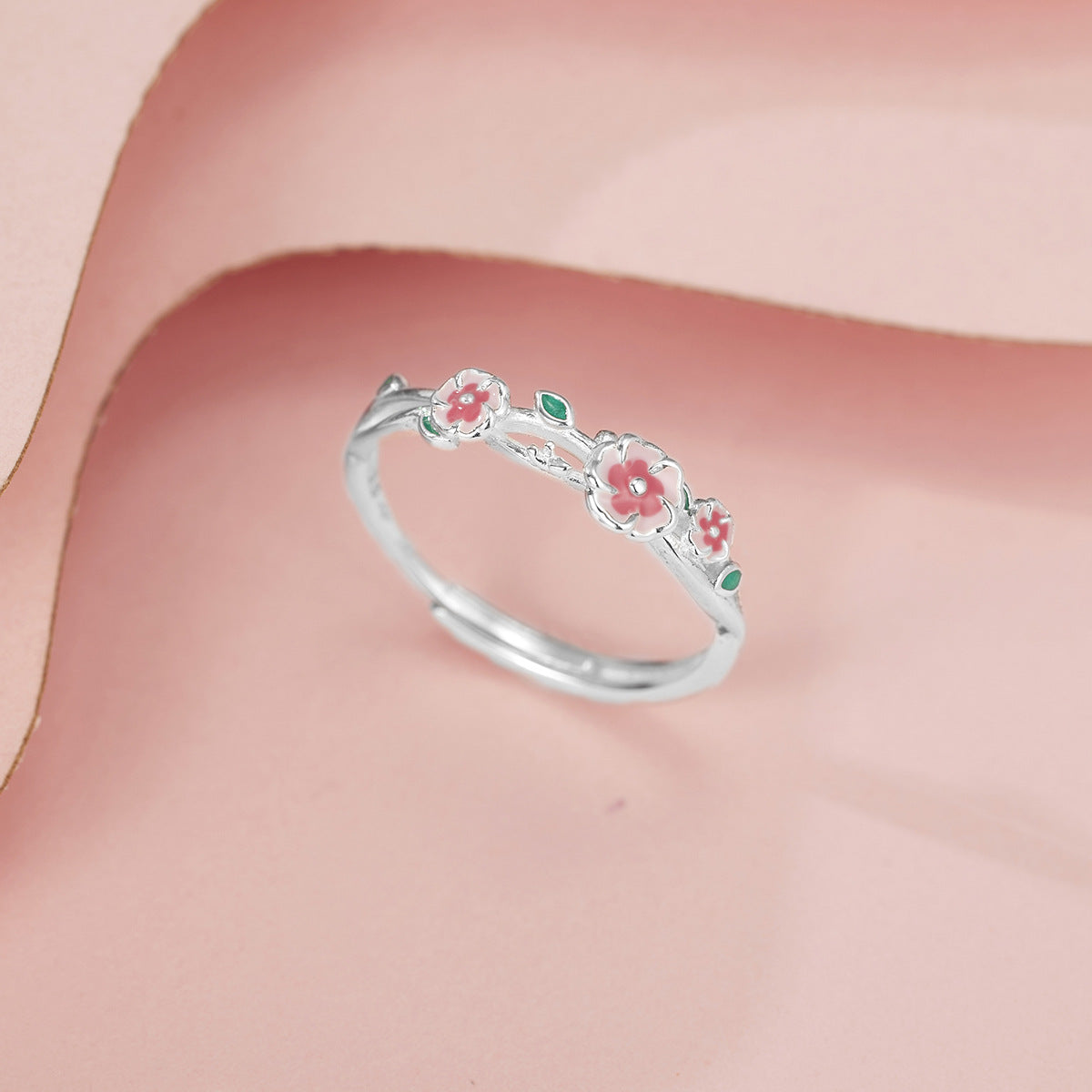 Silver ring with delicate pink flowers and green leaves, adjustable band.