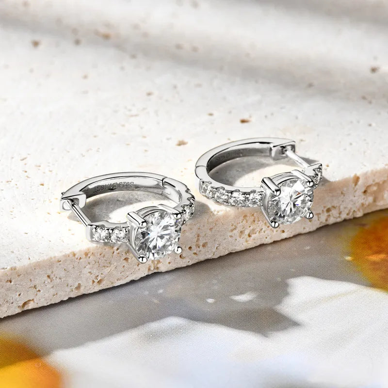 Silver pavé-set moissanite huggie hoop earrings with a central round-cut stone.