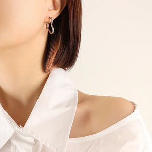 Silver heart huggie earrings made of steel, worn by a woman in a white shirt.