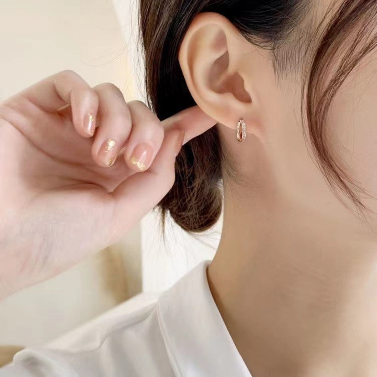 Delicate rose gold hoop earrings with small clear stones, worn by a woman.