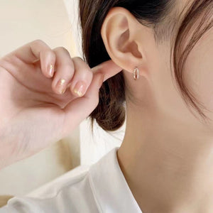 Delicate rose gold hoop earrings with small clear stones, worn by a woman.