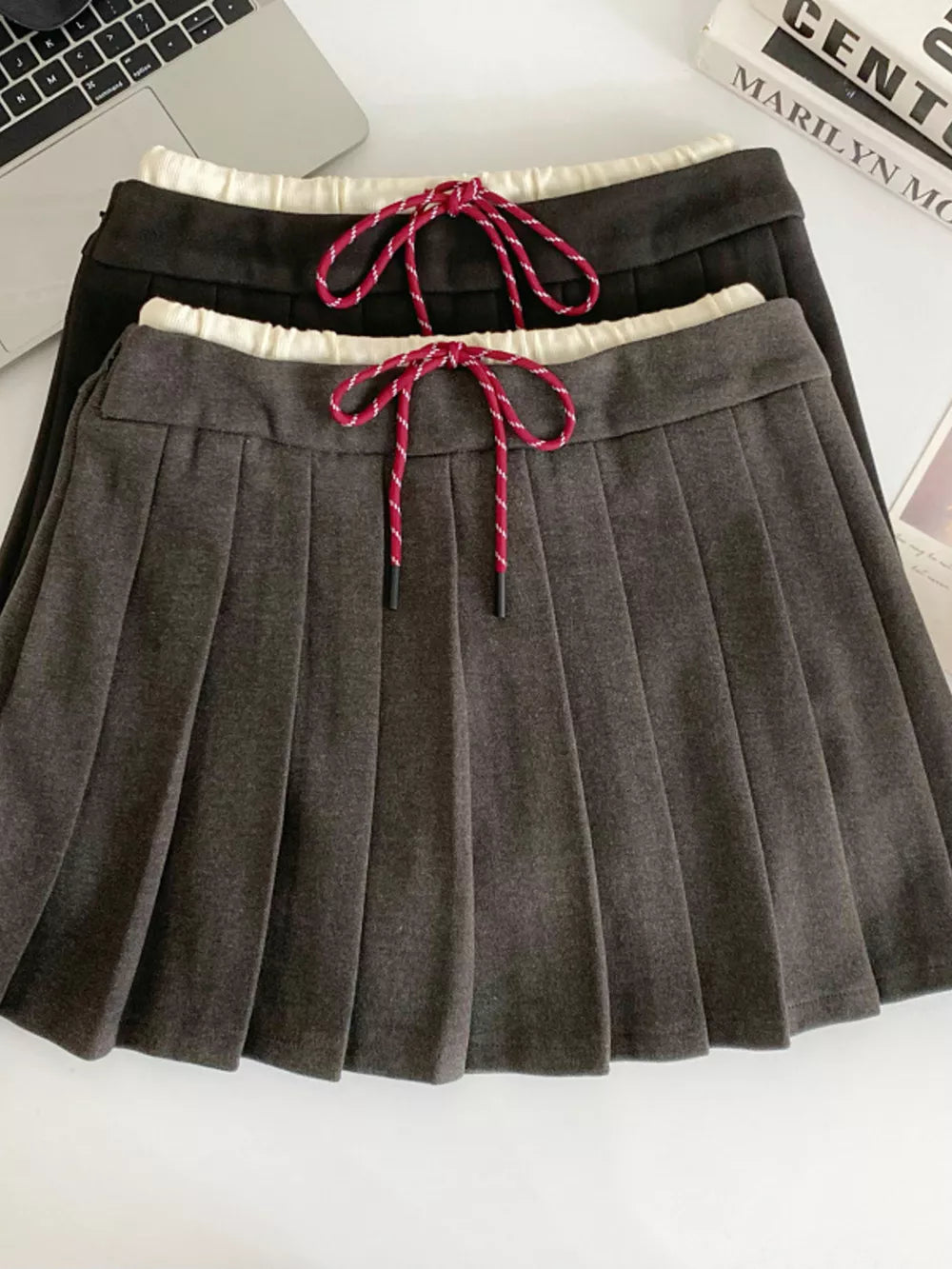 Chic drawstring pleated skirt in dark gray and black with red and white drawstrings.
