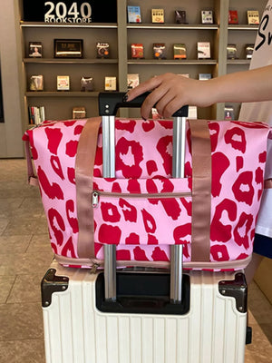 Vibrant leopard print travel bag with pink and red pattern, two handles, and front zipper pocket.