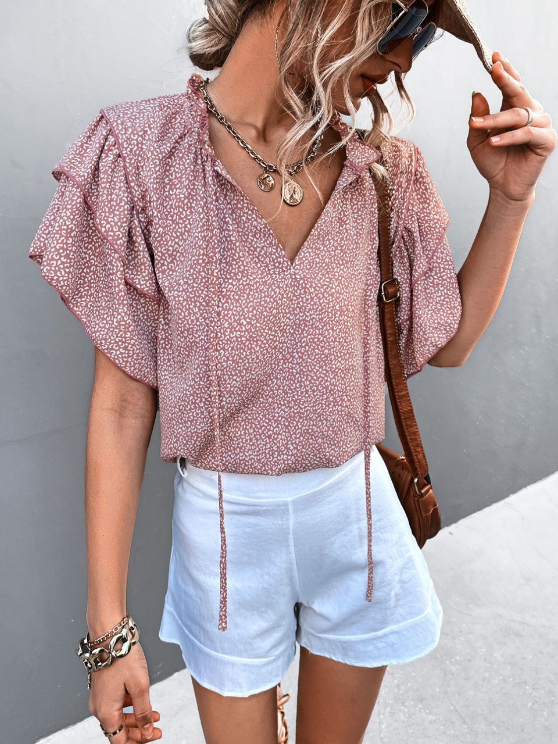 Pink ditsy print blouse with ruffle sleeves and tie neck, styled with white shorts.