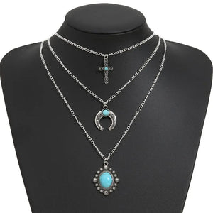 Silver layered necklace with cross, crescent moon, and turquoise pendant.