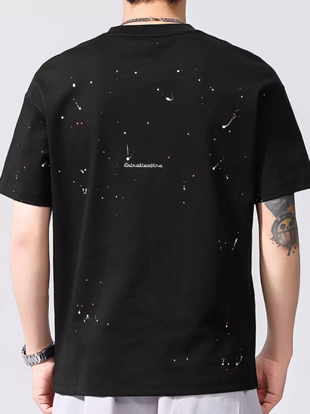 Black cotton t-shirt with artistic white and pink paint splatter pattern, crew neck, short sleeves.