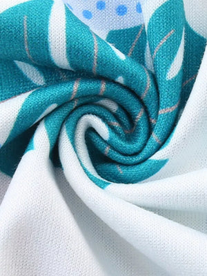 Baby dress in white cotton with teal tropical leaf print and blue polka dots.