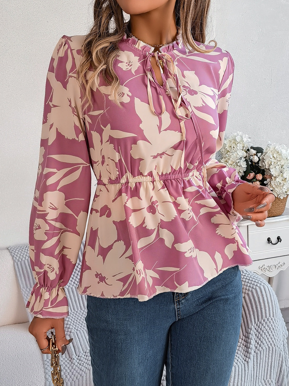 Floral peplum blouse with ruffled neck and tie detail in pink purple, cinched waist, long sleeves.