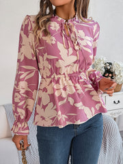 Floral peplum blouse with ruffled neck and tie detail in pink purple, cinched waist, long sleeves.