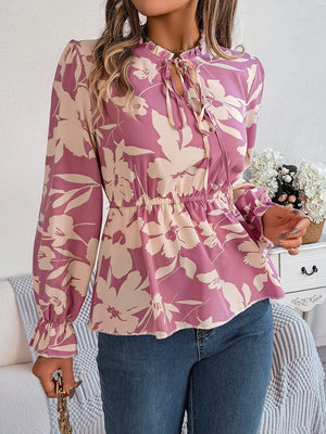 Floral peplum blouse with ruffled neck and tie detail in pink purple, cinched waist, long sleeves.