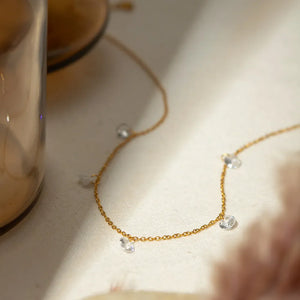 Gold dangling crystal station necklace with delicate chain and scattered clear stones.