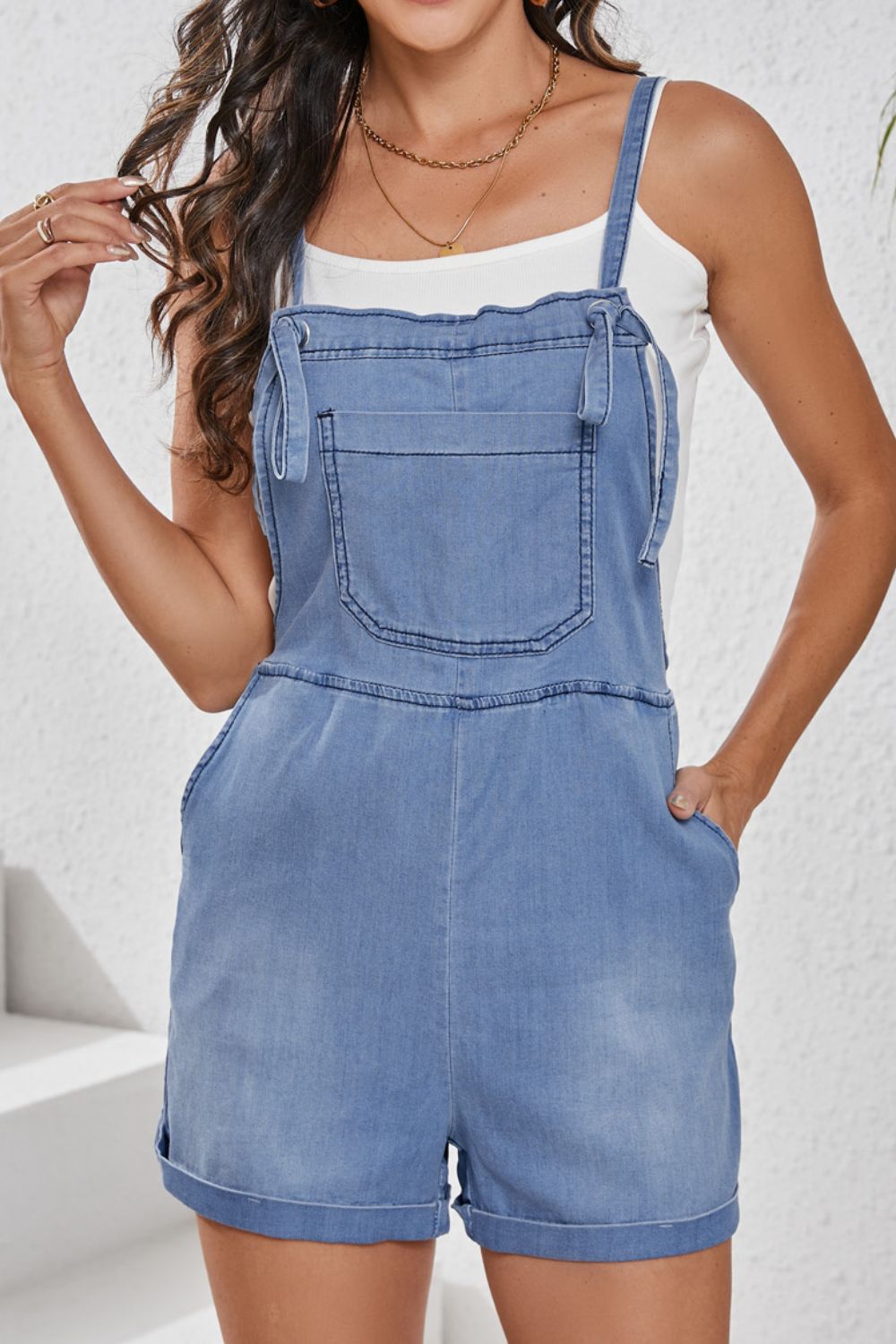 Medium wash denim romper with adjustable straps and cuffed shorts.