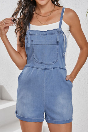 Medium wash denim romper with adjustable straps and cuffed shorts.