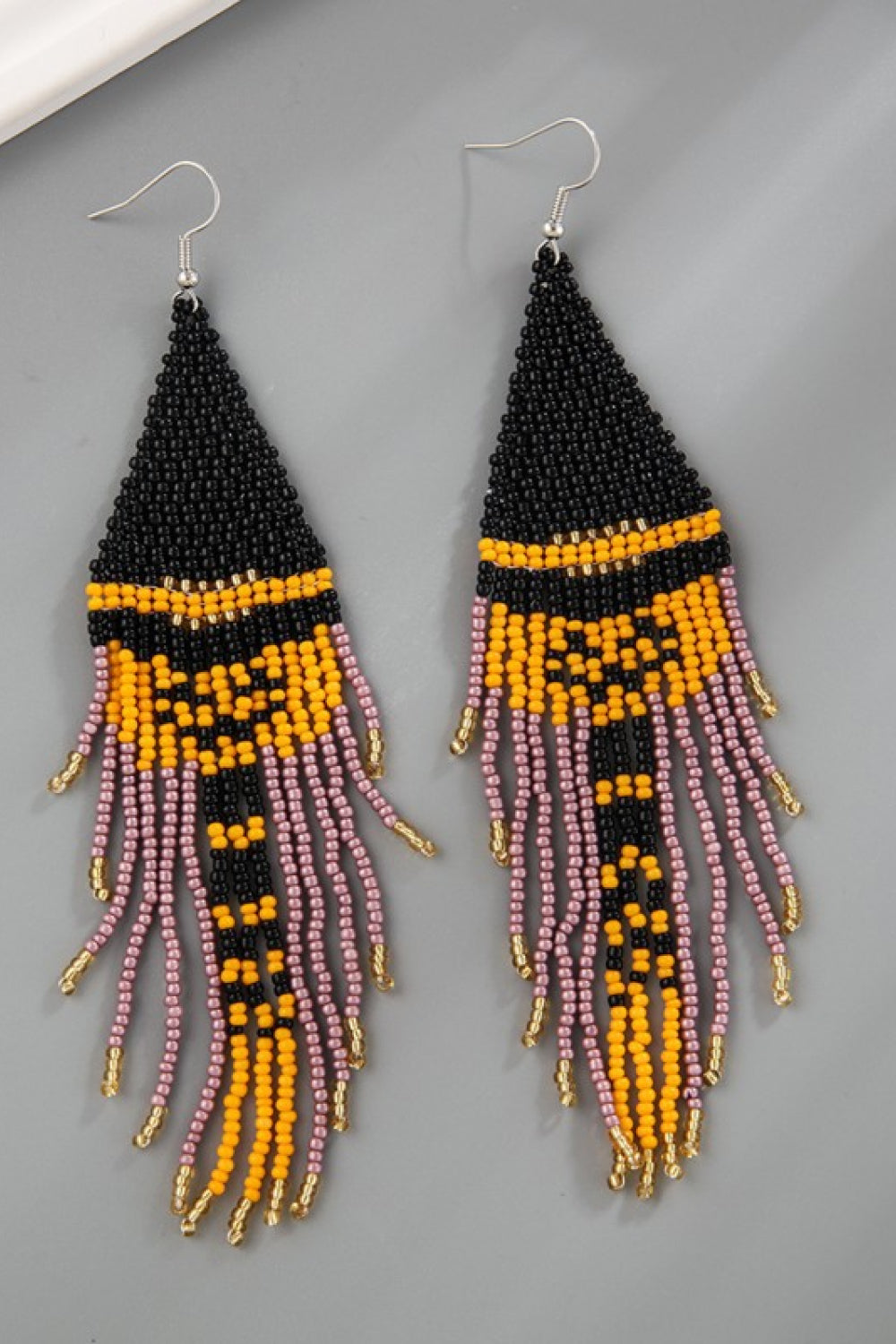 Beaded skull fringe earrings in black, orange, and pink with gold accents.