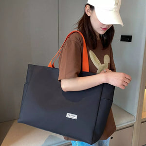 Spacious black canvas shoulder bag with bold orange straps and a small "Fashion" logo tag.